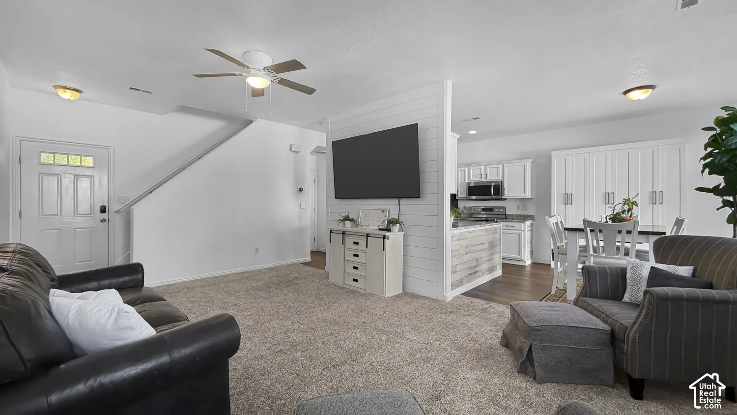Open-concept living area featuring a ceiling fan, carpet flooring, and a partial shiplap wall
