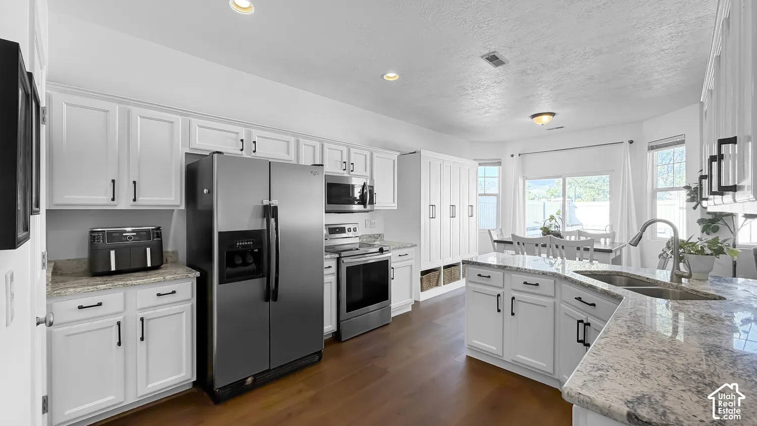 White cabinetry with black hardware, wood-finish flooring, stainless steel appliances, speckled stone countertops, and a double basin sink with a gooseneck faucet