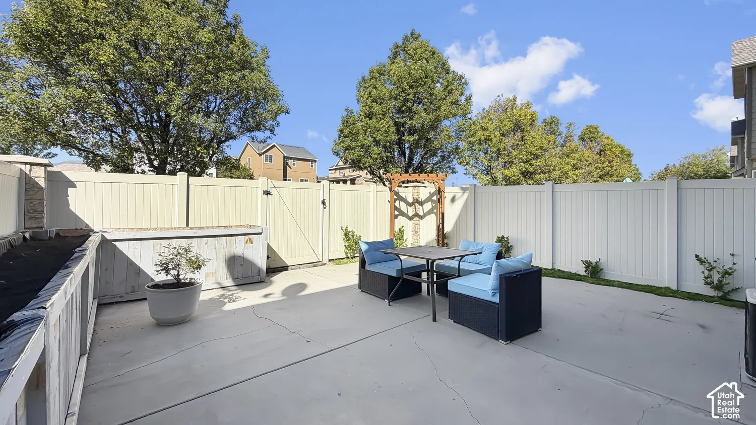 Paved patio space featuring a perimeter fence, raised planter box, and an ornamental trellis