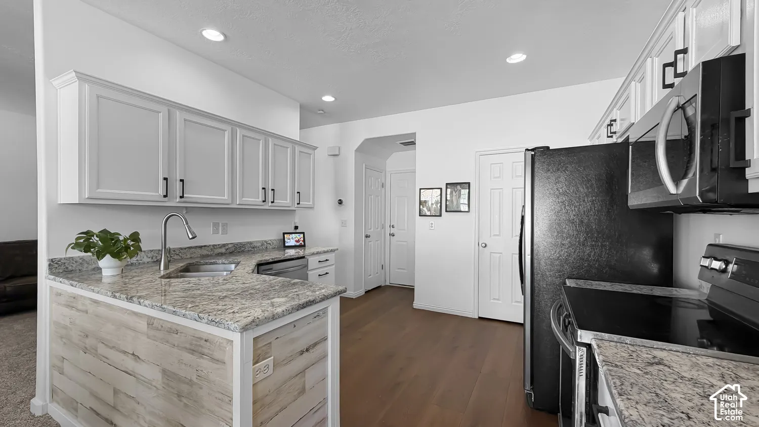 White shaker cabinetry with black hardware, granite countertops, wood-finish flooring, recessed lighting, and black appliances
