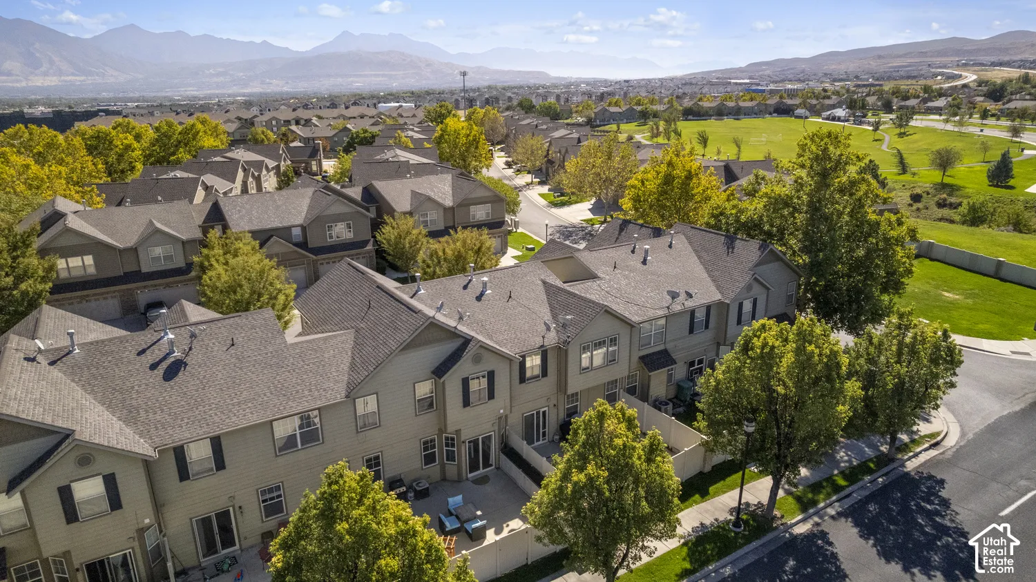 Residential community featuring townhomes with light-colored siding, a shared paved road, mature trees, and distant mountain scenery