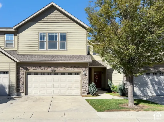 Two-story residence featuring light-colored siding, a stone facade, a two-car garage, and a concrete driveway