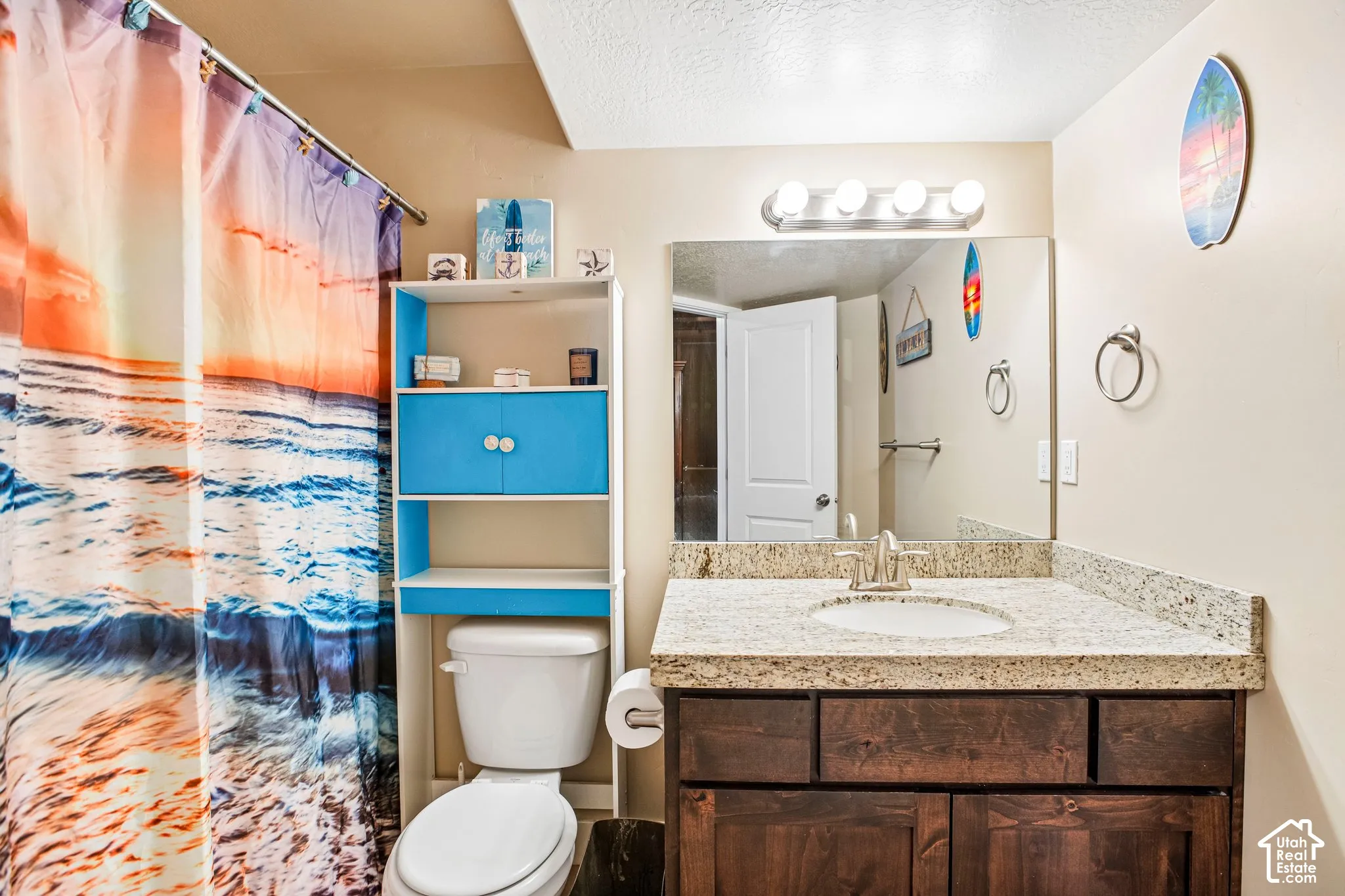 Granite-finish countertop with an undermount sink, dark wood-finish vanity cabinetry, and a framed mirror with a four-bulb light fixture
