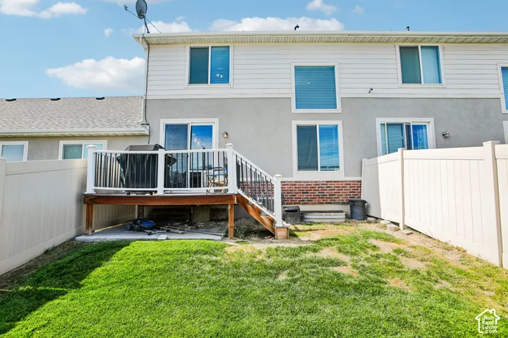 White vinyl fencing, ground-level green space, elevated deck with white railing, sliding glass door access, and a brick accent wall