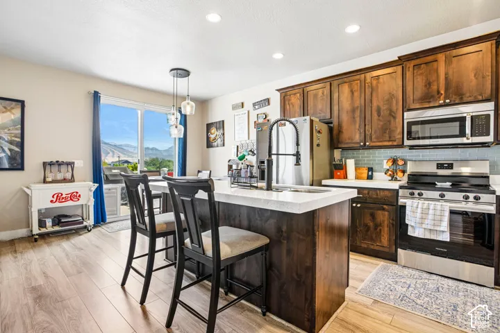 Kitchen featuring stainless steel appliances, wood-finish flooring, dark wood cabinetry, a center island with seating, and a glass sliding door