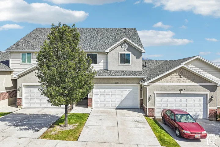 Two-story residence featuring a gray shingle roof, light stucco exterior, white siding accents, and a two-car garage with panel doors