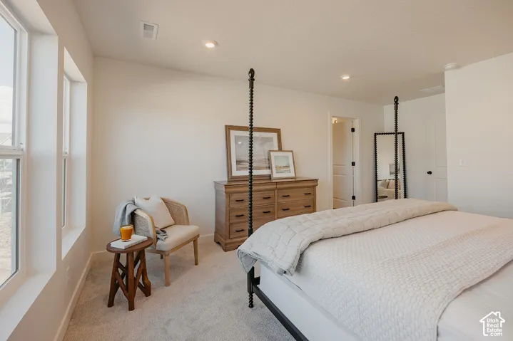 Recessed lighting, light-colored carpet, white walls, multiple windows, and a doorway with a solid panel door