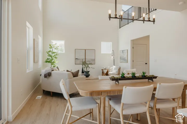 Double-height ceiling, light wood-finish flooring, multiple windows, contemporary chandelier, and a black metal staircase railing