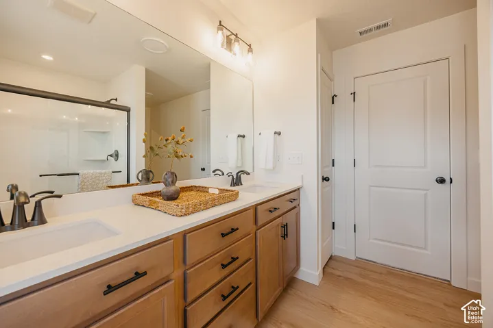 Dual vanity with integrated sinks, light wood-finish cabinetry, sleek black hardware, and a framed glass shower enclosure