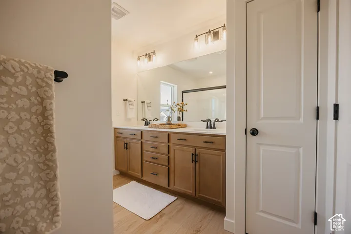 Dual vanity with matte black hardware, integrated sinks, light wood-finish cabinetry, and overhead sconce lighting