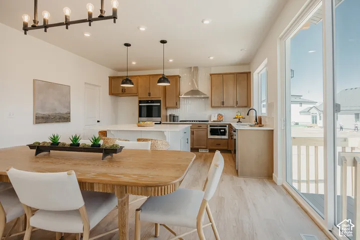 Open-concept living space with wood-finish flooring, a contemporary chandelier, recessed lighting, and a modern kitchen featuring wood cabinetry, stainless steel appliances, and a tile backsplash