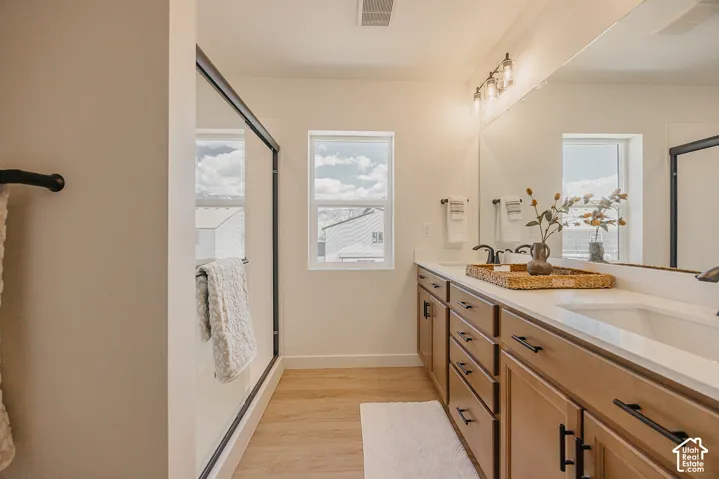 Dual vanity with integrated sinks, wood-finish cabinetry, a large frameless mirror, and modern three-bulb vanity lighting
