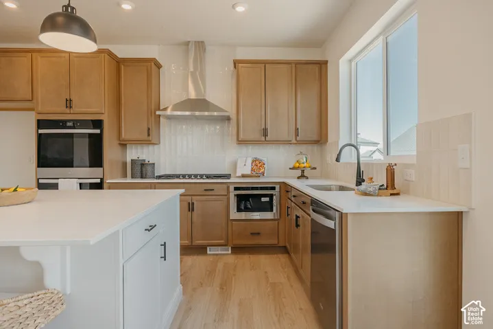 Kitchen featuring light wood-finish cabinetry, stainless steel appliances, a white solid surface countertop, and wood-finish flooring