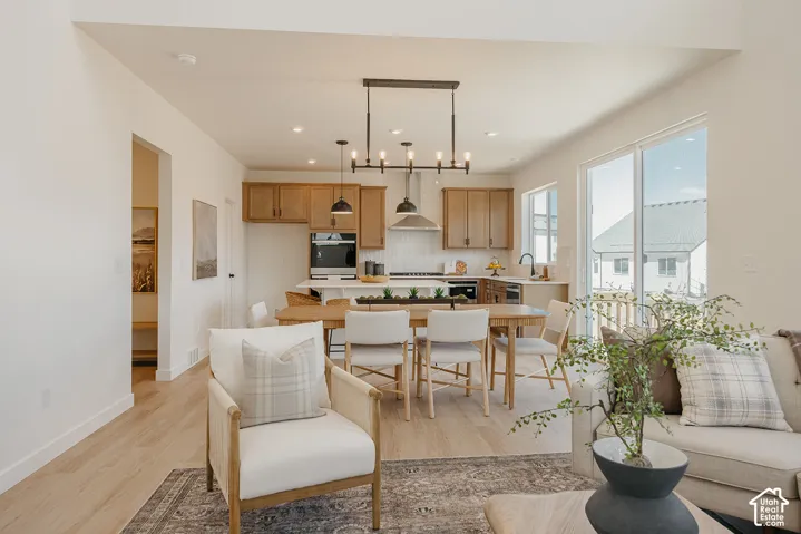 Open-concept living area featuring wood-finish flooring, a kitchen with light wood cabinetry, white countertops, and a white tiled backsplash