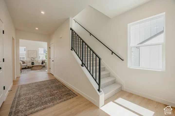 Wood-finish flooring with recessed lighting, a carpeted staircase featuring a black metal railing, and a window with white trim