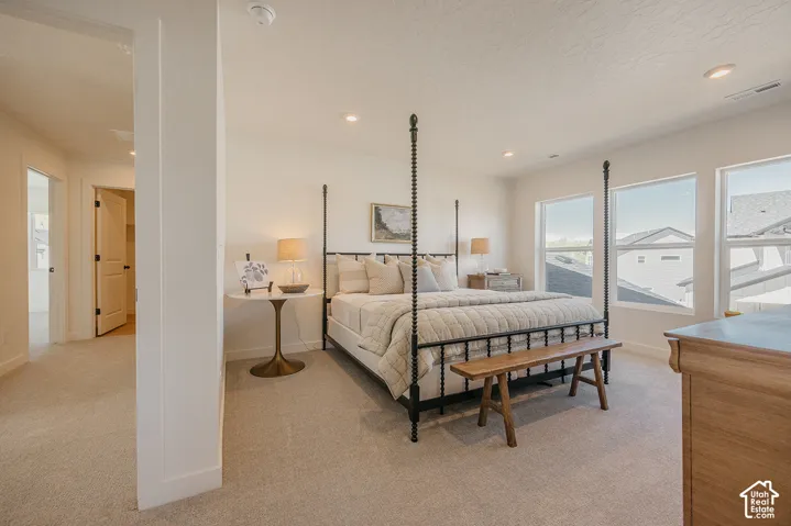 Recessed lighting illuminates neutral carpeting and a hallway with a solid core door