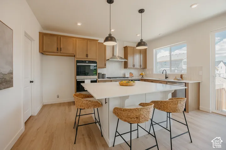 Contemporary kitchen featuring wood-finish flooring, a spacious center island with seating, built-in double ovens, and recessed lighting