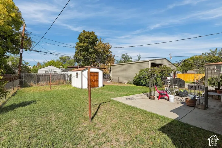 Expansive backyard featuring a grass lawn, concrete patio, and two storage sheds