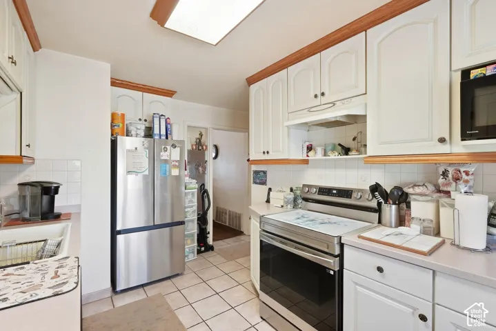 White cabinetry with wood trim, stainless steel appliances, and white tile flooring