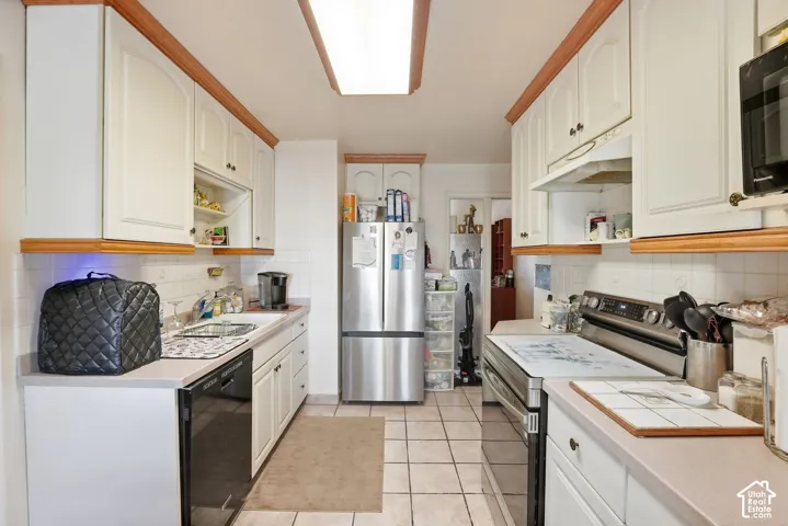 Galley kitchen featuring white cabinetry with wood trim, white tile flooring, and a subway tile backsplash