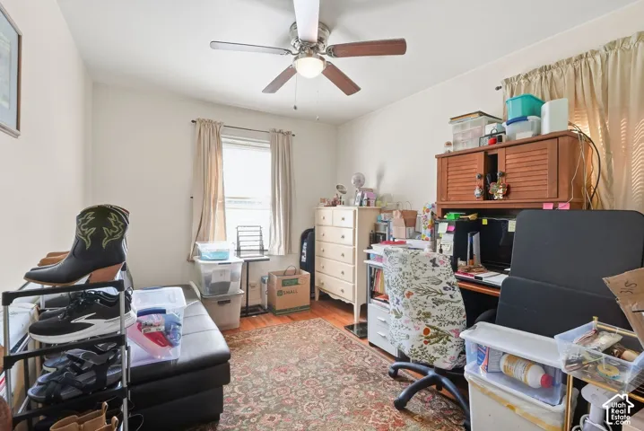Ceiling fan with light fixture, single window with drapes, wood-finish flooring