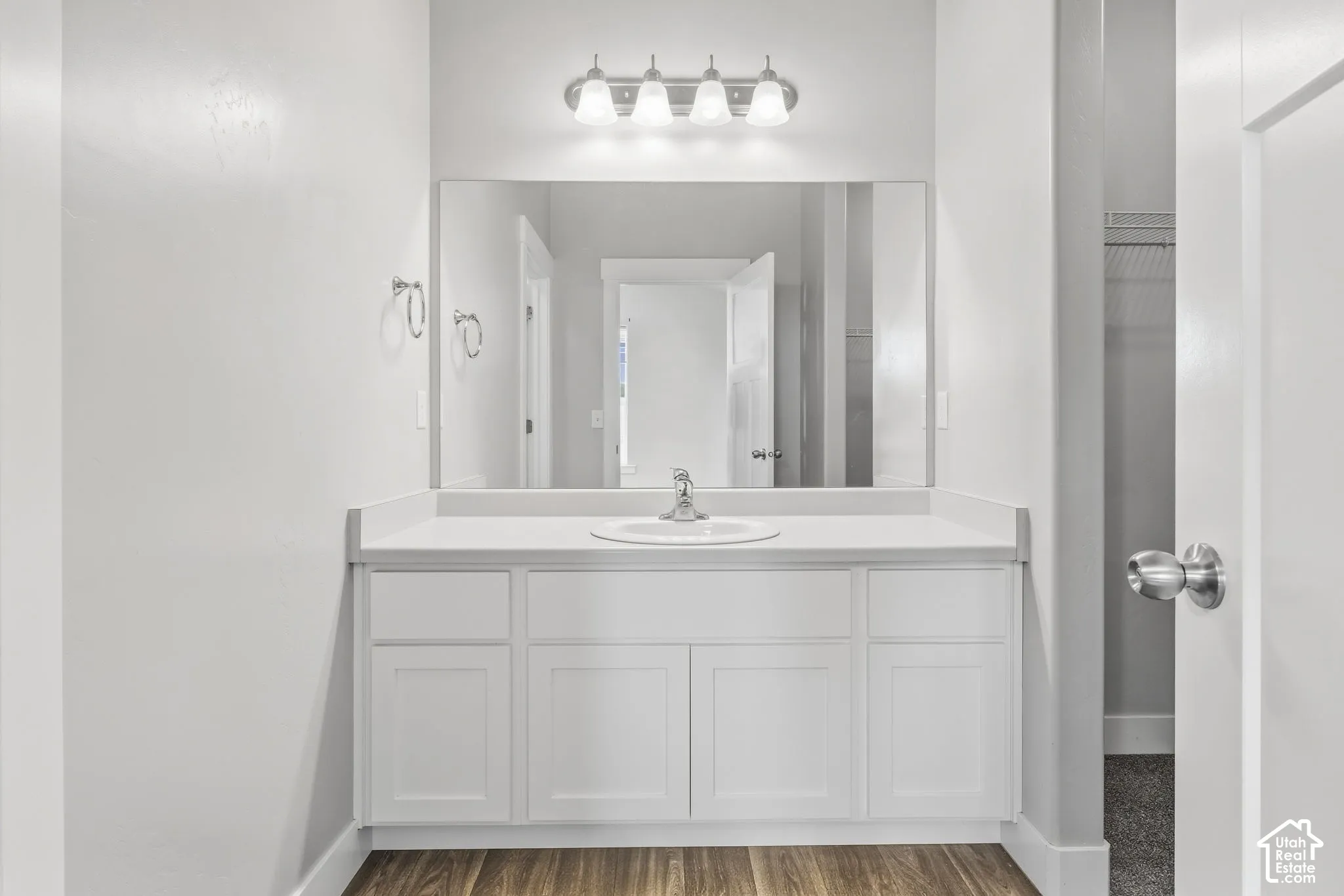 White shaker-style cabinetry with a single basin sink, light-toned countertop, and integrated vanity lighting