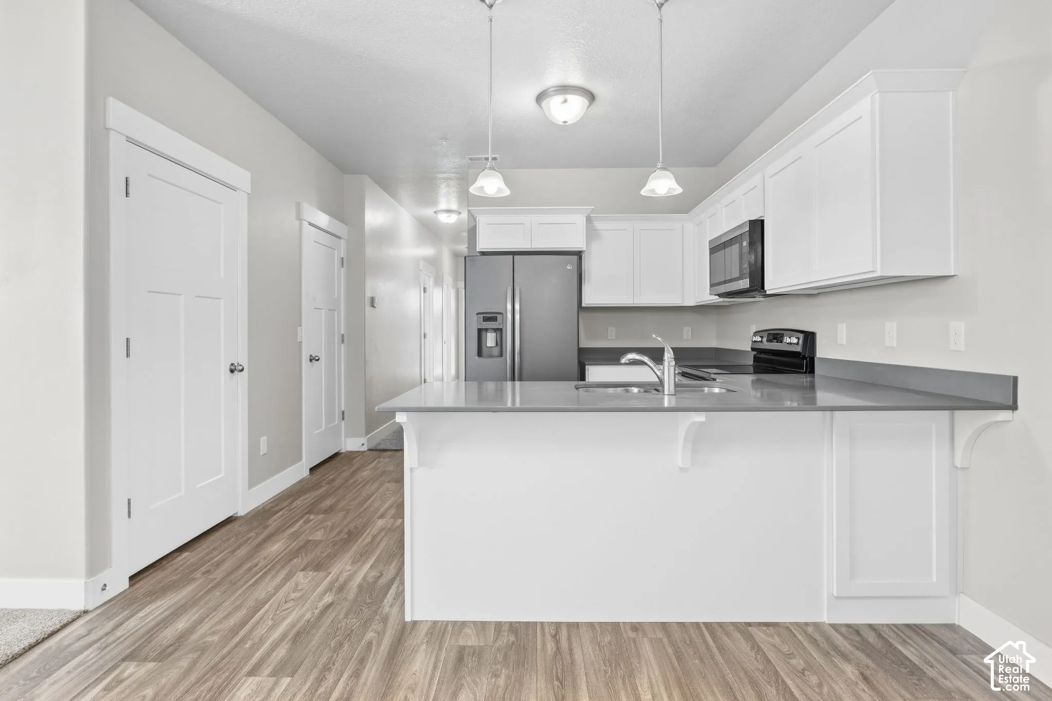 Modern kitchen featuring white cabinetry, stainless steel appliances, a kitchen island with seating, dark countertops, and wood-finish flooring
