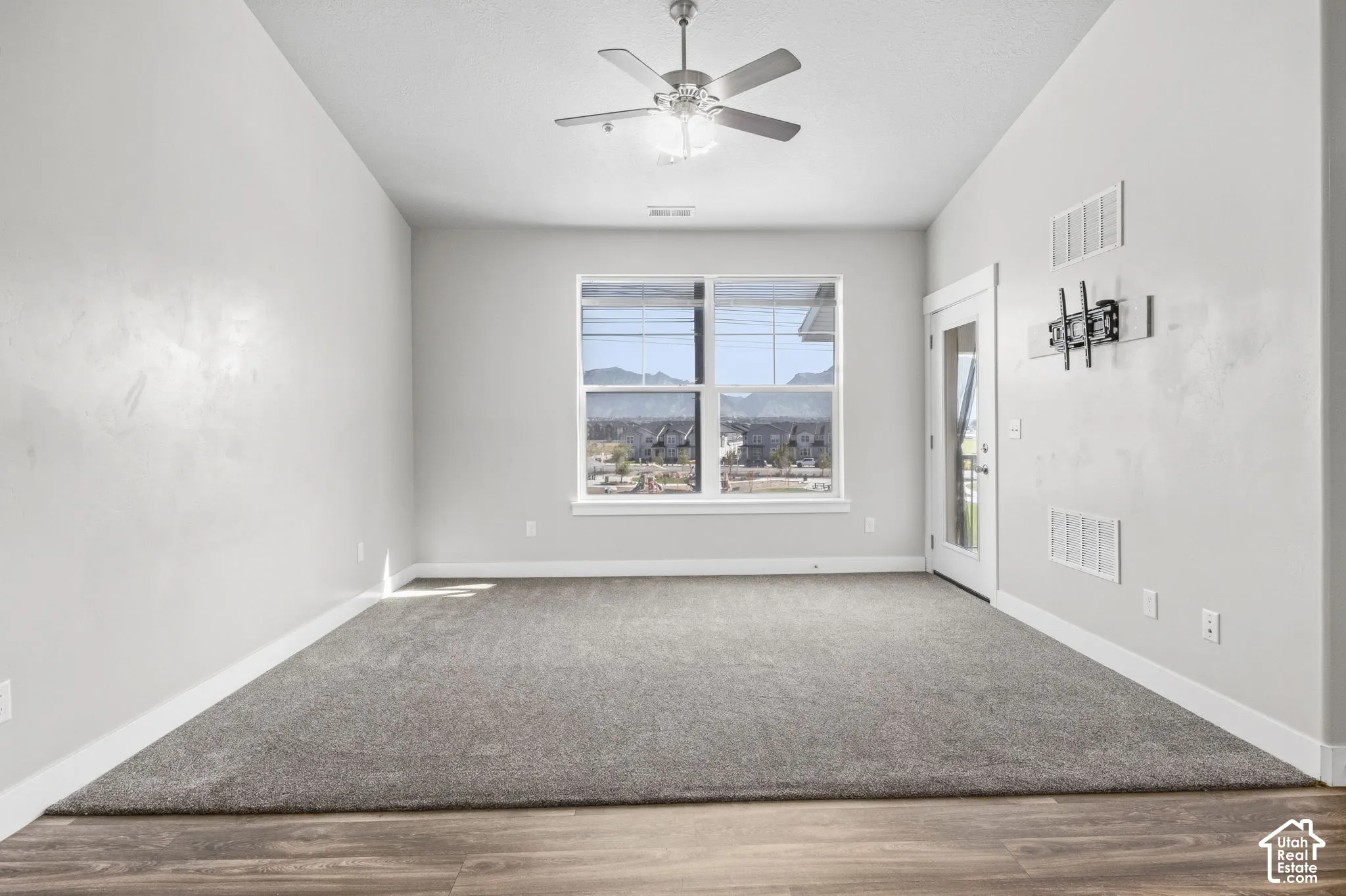 Wood-finish flooring with a carpet inlay, large window, white trim, ceiling fan with integrated lighting, and a glass-paneled door
