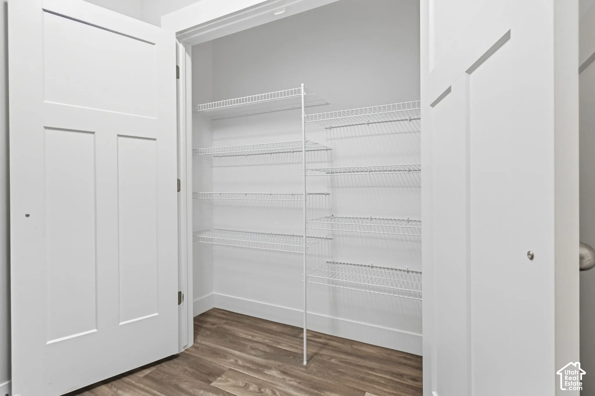 White shaker-style doors open to a spacious pantry featuring multiple tiers of wire shelving and wood-finish flooring
