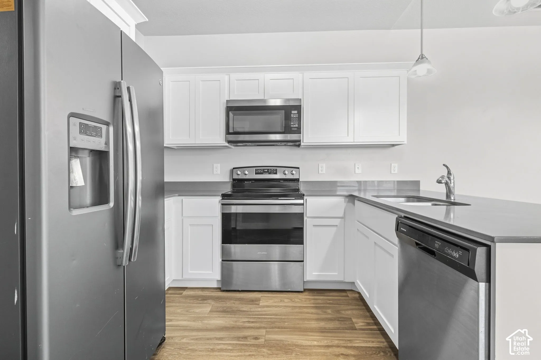 Kitchen featuring white cabinetry, gray countertops, stainless steel appliances, and wood-finish flooring