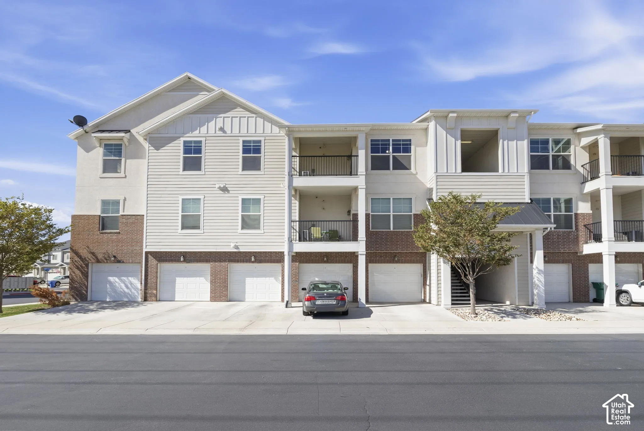 Multi-level building with brick and siding exterior, private balconies, and integrated garages