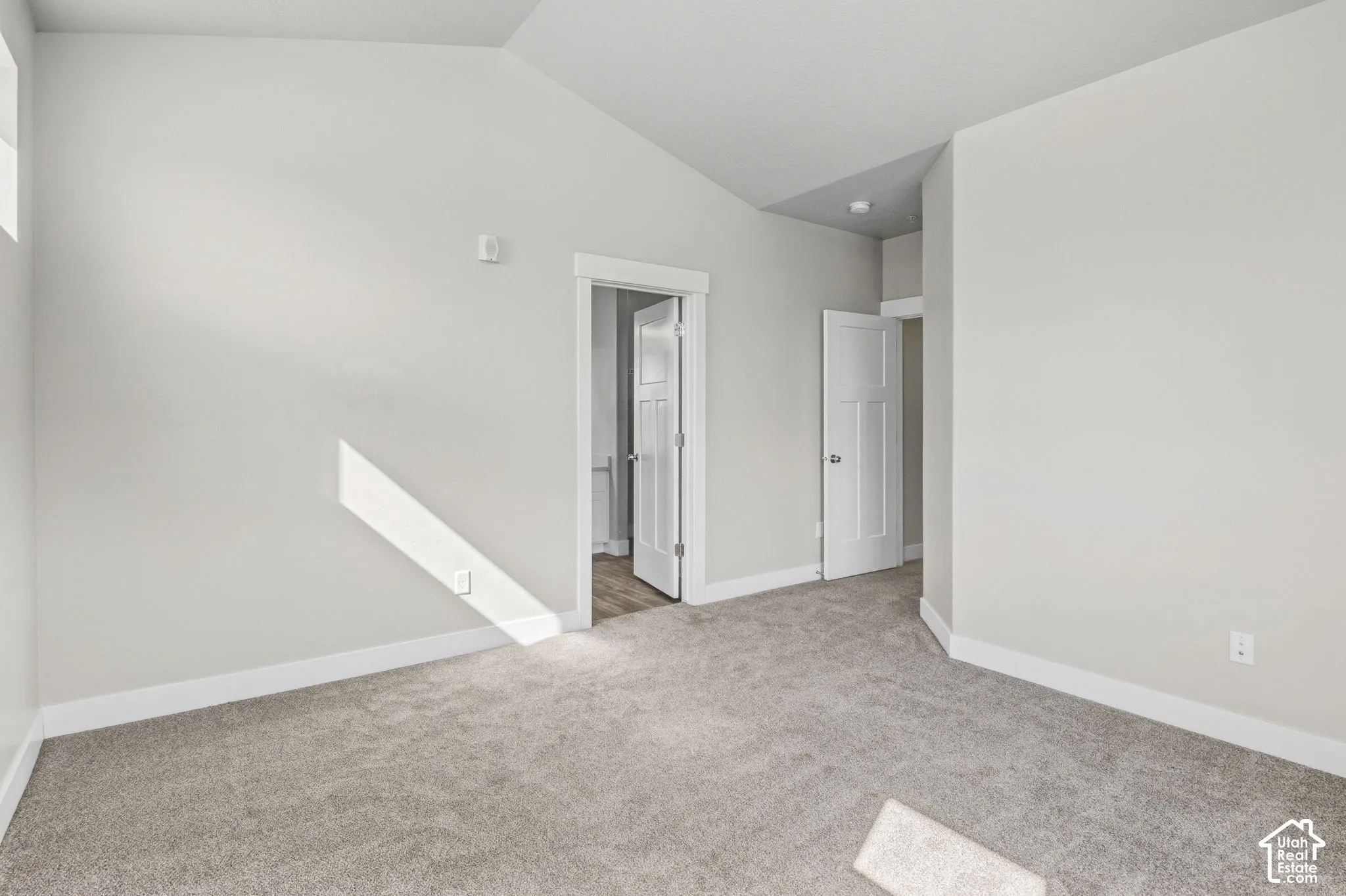 Vaulted ceiling with an overhead light fixture, light gray carpeting, neutral wall paint, and white trim