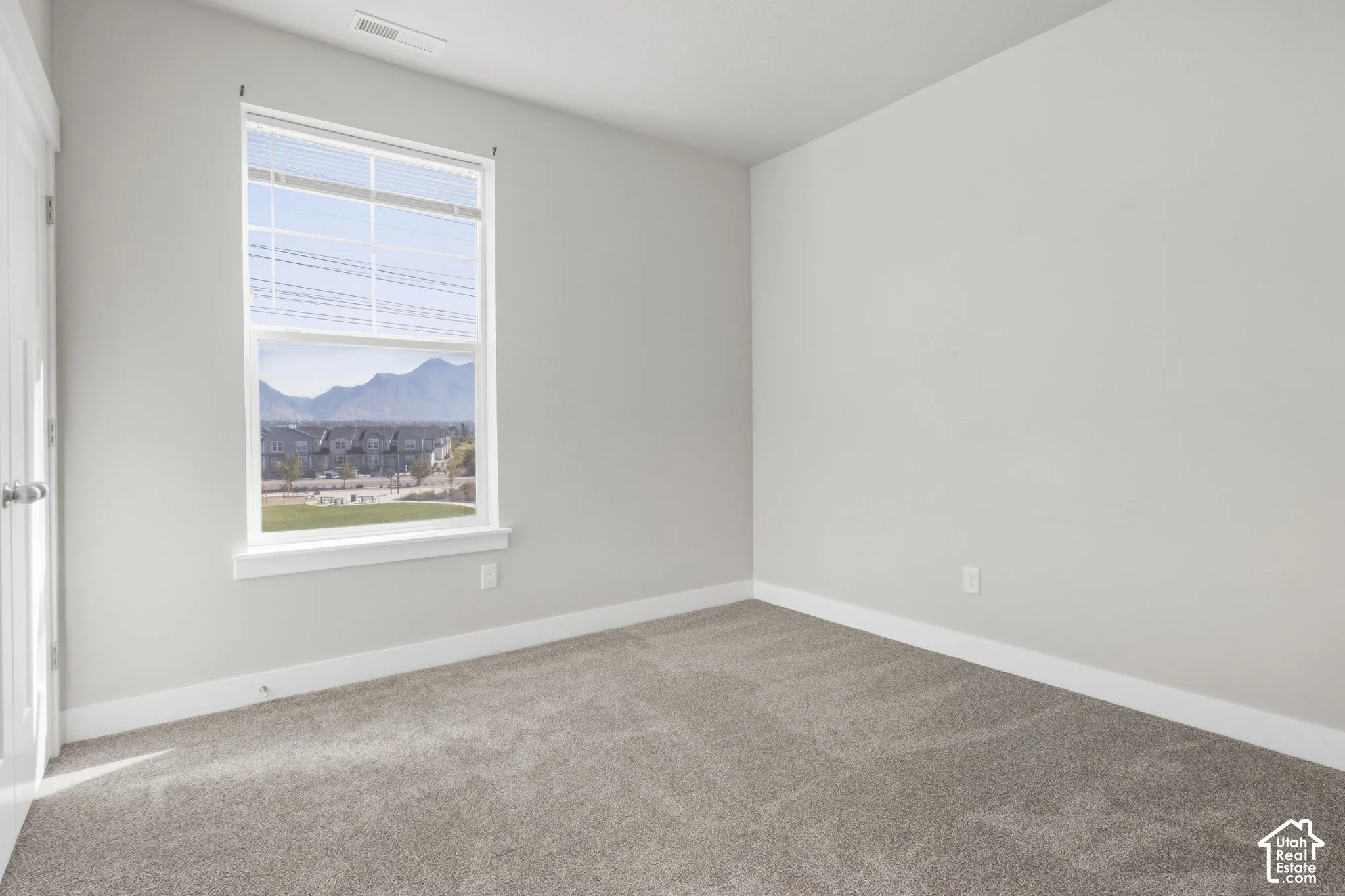 Neutral tone walls, plush carpet flooring, white trim, and a window with mountain scenery