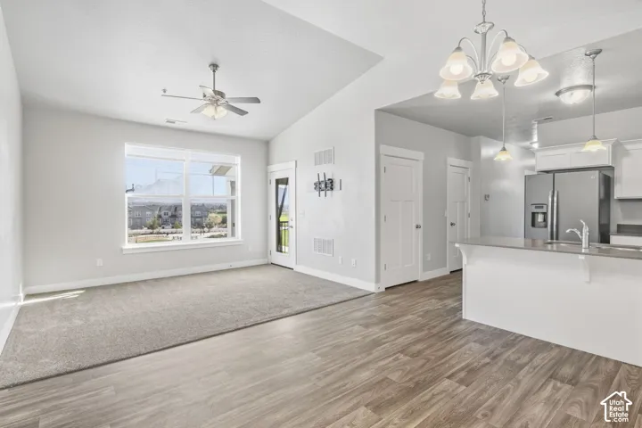 Vaulted ceiling with ceiling fan, large picture window, wood-finish flooring, built-in kitchen island, and stainless steel appliances