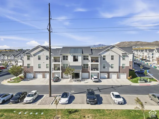 Three-story multi-unit structure featuring brick and horizontal siding, individual garages, private balconies, and dedicated parking