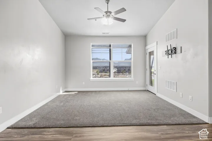 Wood-finish flooring with a carpet inlay, large window, white trim, ceiling fan with integrated lighting, and a glass-paneled door