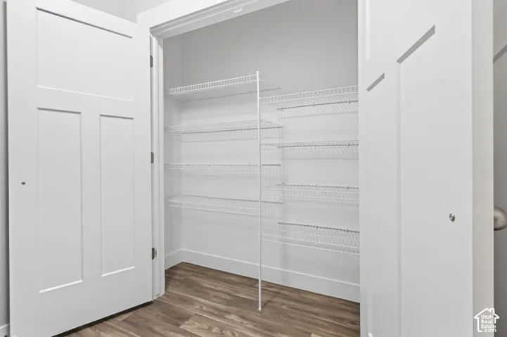 White shaker-style doors open to a spacious pantry featuring multiple tiers of wire shelving and wood-finish flooring