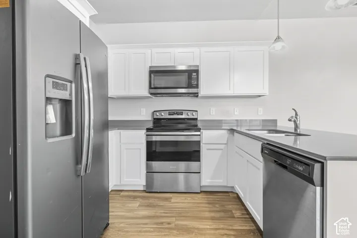 Kitchen featuring white cabinetry, gray countertops, stainless steel appliances, and wood-finish flooring