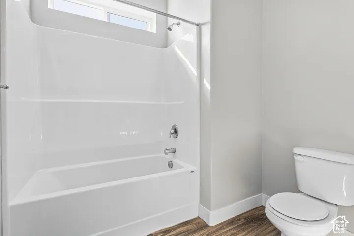 White tub and shower combination with chrome fixtures, a privacy window, and wood-finish flooring