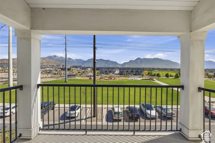 Covered balcony with black metal railings overlooking expansive green space and distant mountains