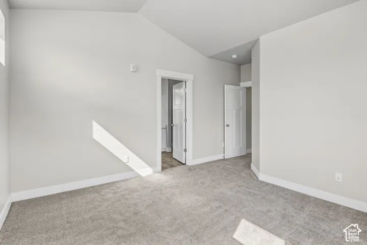 Vaulted ceiling with an overhead light fixture, light gray carpeting, neutral wall paint, and white trim