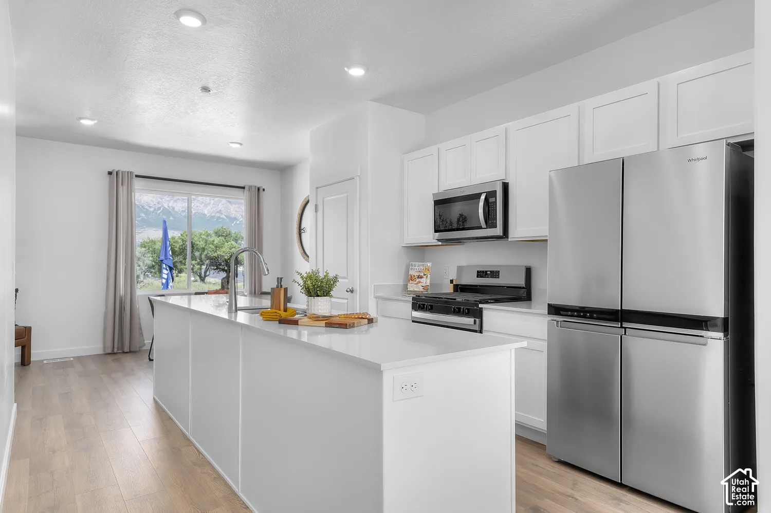 Bright kitchen featuring a center island, recessed lighting, wood-finish flooring, white cabinetry, and stainless steel appliances