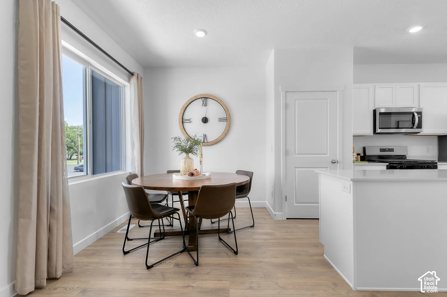 Open-concept dining area featuring wood-finish flooring, recessed lighting, and a window with a dark rod