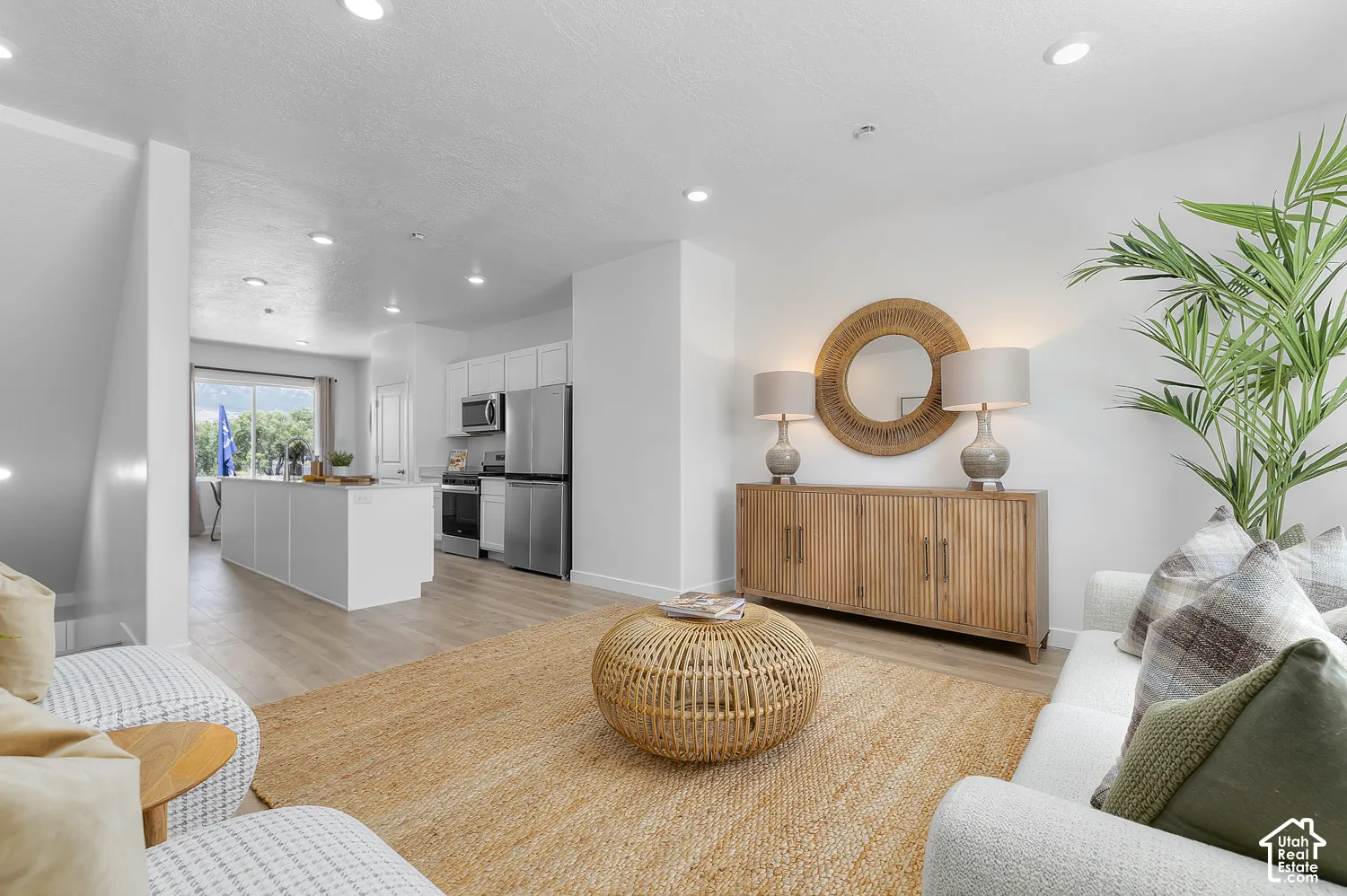 Open-concept living space featuring wood-finish flooring, recessed lighting, and a kitchen with stainless steel appliances, white cabinetry, and a central island