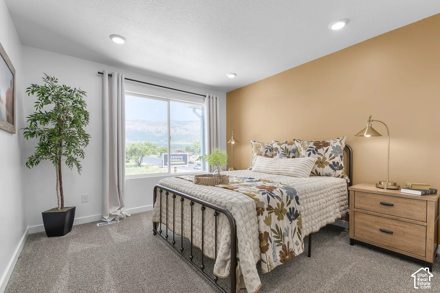 Recessed ceiling lighting illuminates the room with a large window and gray carpeting