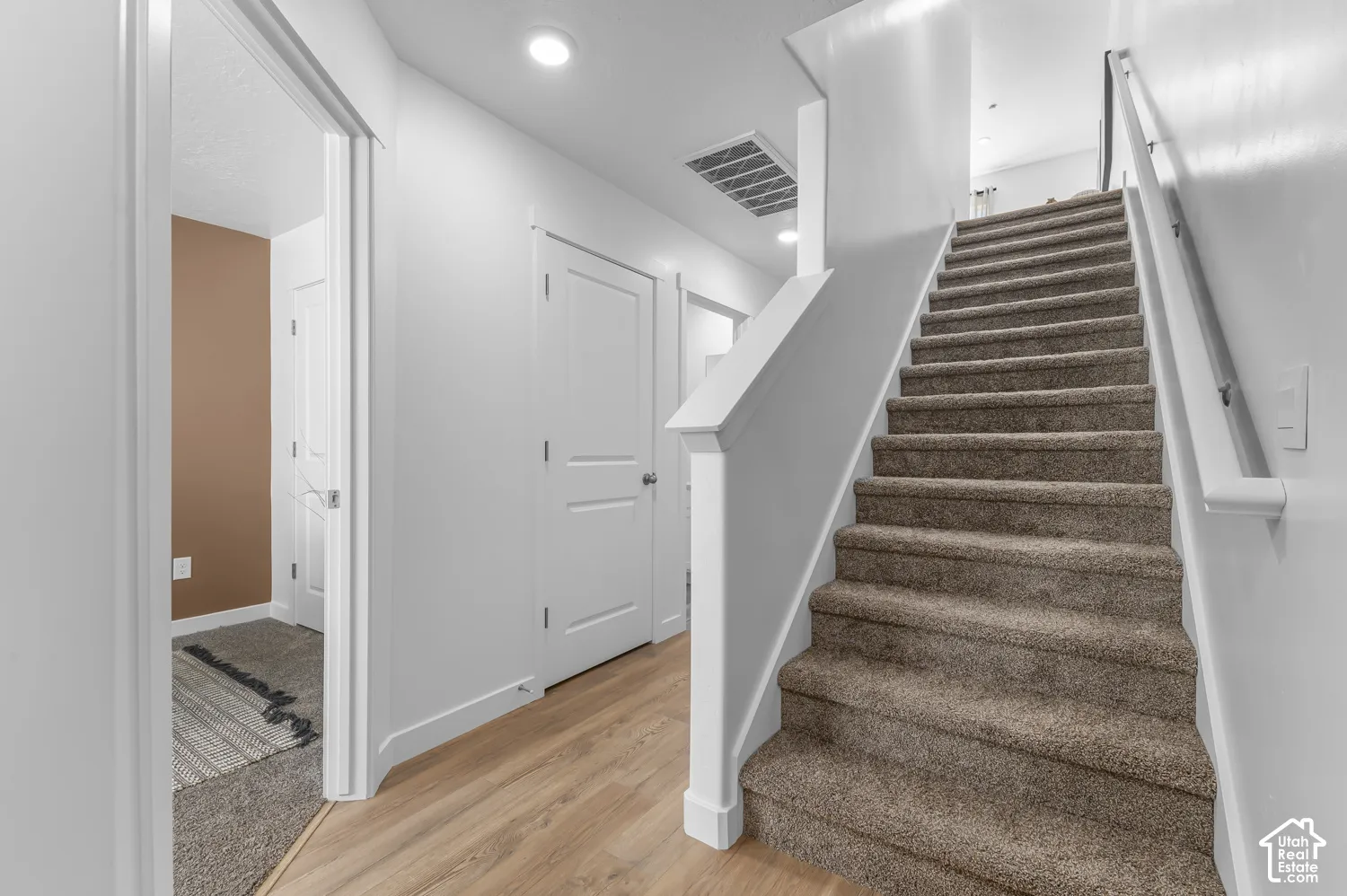 Carpeted staircase with white handrails, wood-finish flooring, recessed lighting, and white paneled doors