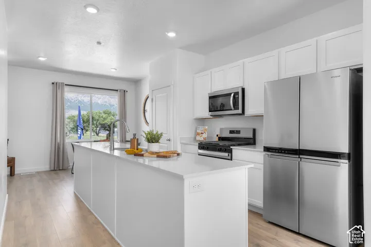 Bright kitchen featuring a center island, recessed lighting, wood-finish flooring, white cabinetry, and stainless steel appliances