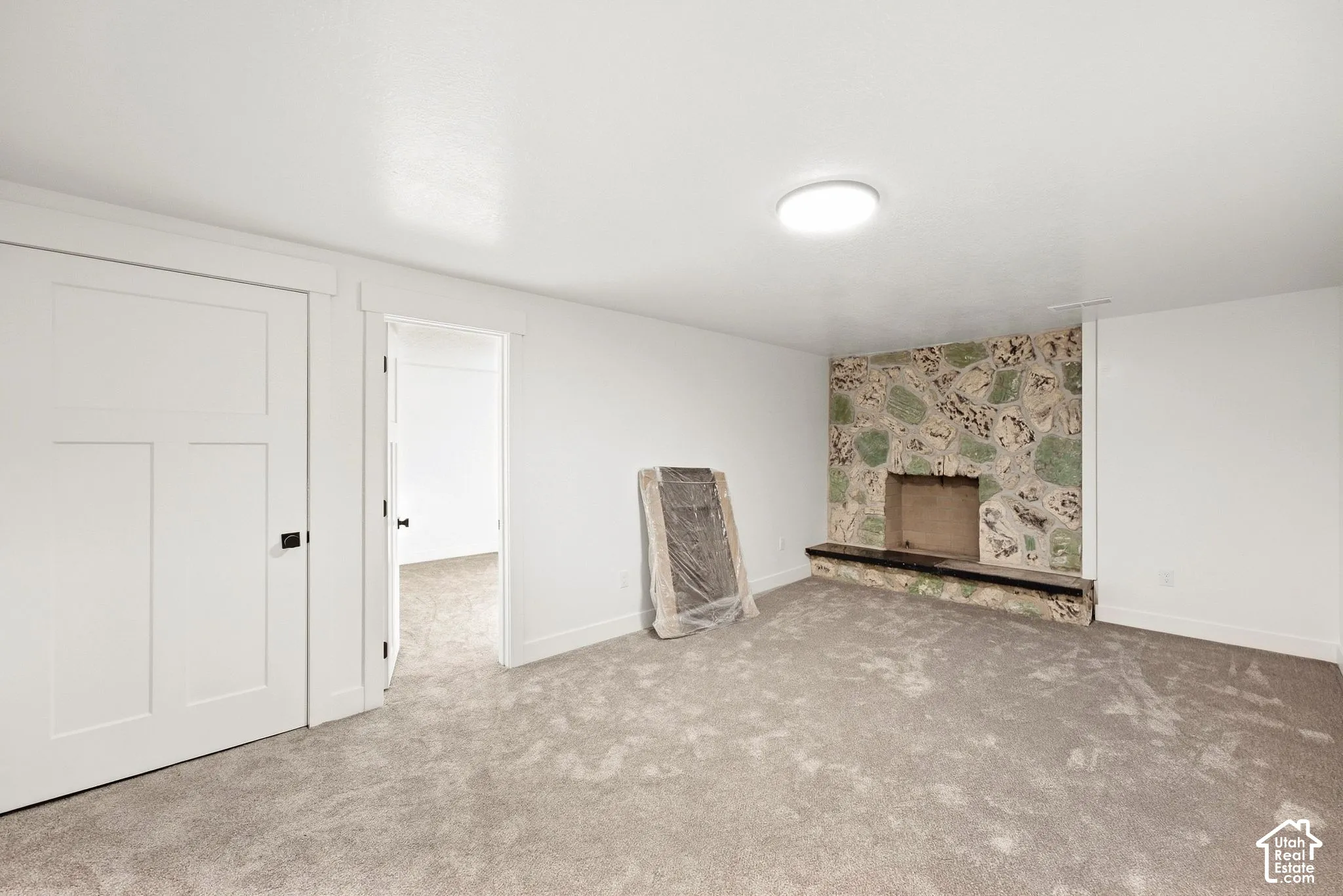 Textured stone fireplace with a raised hearth, light gray carpeting, and white interior doors with black hardware