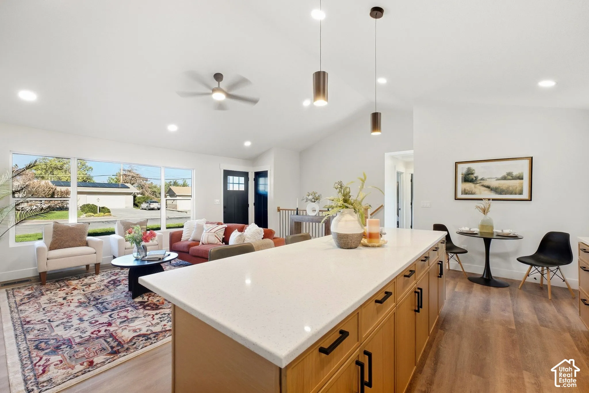 Vaulted ceilings with recessed lighting, wood-finish flooring, a kitchen island with a light-toned countertop, and a built-in ceiling fan