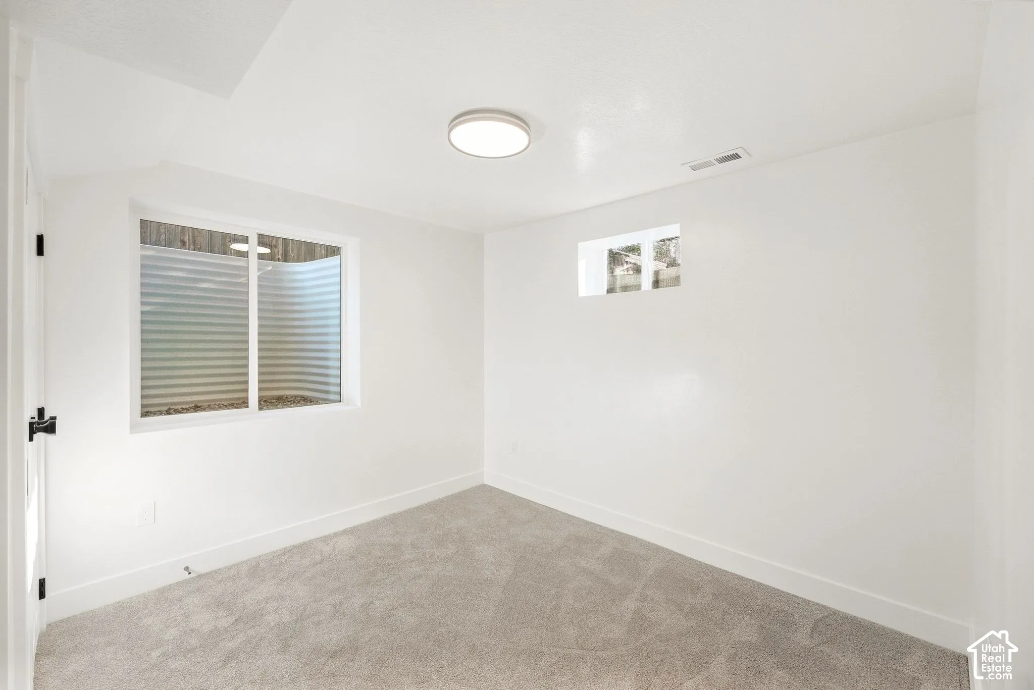 White walls, plush carpeting, and two windows provide natural light